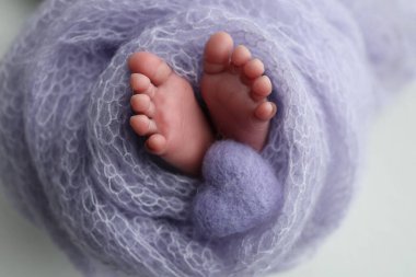 Yeni doğmuş bir bebeğin küçük ayağı. Mor yün battaniyeli leylak rengi bir bebeğin yumuşak ayakları. Ayak parmakları, topuklar ve yeni doğmuş bir bebeğin ayakları. Bir bebeğin bacaklarında örülmüş mor kalp. Makro fotoğrafçılık.