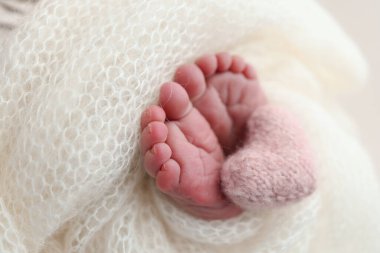 Yeni doğmuş bir bebeğin küçük ayağı. Beyaz yün battaniyenin içinde yeni doğmuş bir bebeğin yumuşak ayakları. Ayak parmakları, topuklar ve yeni doğmuş bir bebeğin ayakları. Bir bebeğin bacaklarında pembe bir kalp örülmüş. Makro fotoğrafçılık 