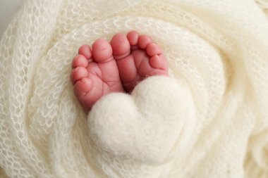 Yeni doğmuş bir bebeğin küçük ayağı. Beyaz yün battaniyenin içinde yeni doğmuş bir bebeğin yumuşak ayakları. Ayak parmakları, topuklar ve yeni doğmuş bir bebeğin ayakları. Bir bebeğin bacaklarında örülmüş beyaz kalp. Makro fotoğrafçılık 