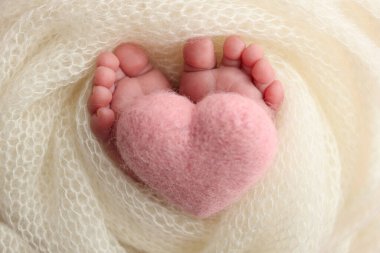 Yeni doğmuş bir bebeğin küçük ayağı. Beyaz yün battaniyenin içinde yeni doğmuş bir bebeğin yumuşak ayakları. Ayak parmakları, topuklar ve yeni doğmuş bir bebeğin ayakları. Bir bebeğin bacaklarında pembe bir kalp örülmüş. Stüdyo makro fotoğrafçılık. 