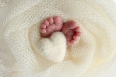 Yeni doğmuş bir bebeğin küçük ayağı. Beyaz yün battaniyenin içinde yeni doğmuş bir bebeğin yumuşak ayakları. Ayak parmakları, topuklar ve yeni doğmuş bir bebeğin ayakları. Bir bebeğin bacaklarında örülmüş beyaz kalp. Makro fotoğrafçılık.