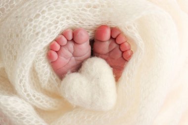 Yeni doğmuş bir bebeğin küçük ayağı. Beyaz yün battaniyenin içinde yeni doğmuş bir bebeğin yumuşak ayakları. Ayak parmakları, topuklar ve yeni doğmuş bir bebeğin ayakları. Bir bebeğin bacaklarında örülmüş beyaz kalp. Makro fotoğrafçılık.