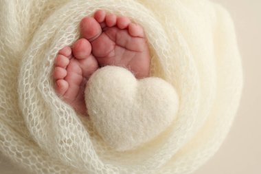 Yeni doğmuş bir bebeğin küçük ayağı. Beyaz yün battaniyenin içinde yeni doğmuş bir bebeğin yumuşak ayakları. Ayak parmakları, topuklar ve yeni doğmuş bir bebeğin ayakları. Bir bebeğin bacaklarında örülmüş beyaz kalp. Makro fotoğrafçılık.