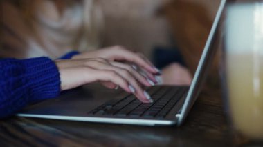 Female freelancers hands with manicure typing on laptop keyboard in cafe.