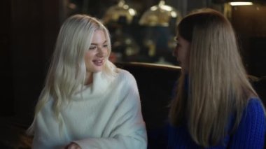 Two women on sofa are hugging and supporting each other at the cafe.