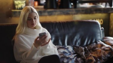 Female friends meeting, girls hug while sitting on sofa in cafe.