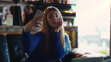 Attractive woman looking at her cell phone and taking a selfie in a modern cafe.