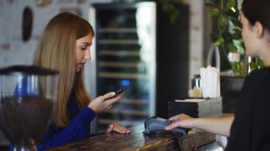 In the cafe woman pays by contactless mobile phone to credit card system, slow motion.