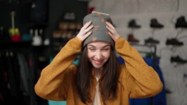 Front view of a smiling woman trying on a new colorful winter hat in a store.