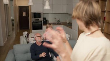 Playful crazy young daddy performing parody to guess together with a family in living room interior.