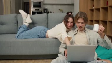 Young adult couple talking using laptop computer at home watching video.