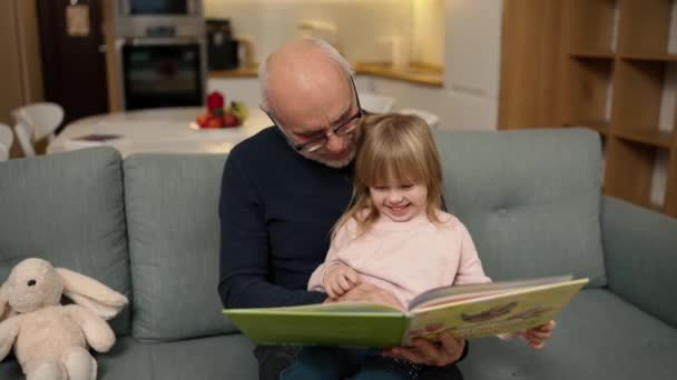 おじいさんは孫娘に本を読んでいます — ストック動画