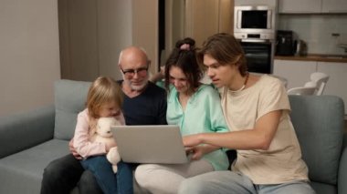 Children and grandpa are laughing together while using a laptop, watching video.