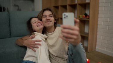 Lovely couple sitting on the floor together, taking selfie with smartphone.