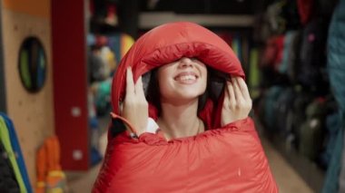 A smiling woman purchase in sportswear store, checking and trying sleeping bag in front camera.