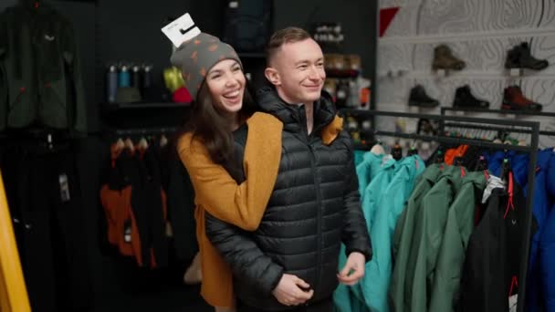 Νεαρός Που Δοκιμάζει Χειμωνιάτικο Μπουφάν Κατάστημα Ρούχων Την Κοπέλα Του — Αρχείο Βίντεο