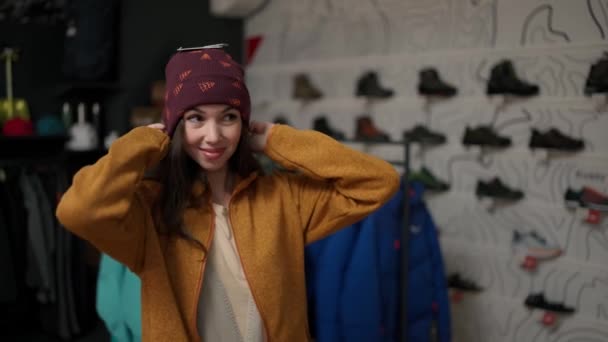 笑顔の女性は店で新しいカラフルな冬の帽子をしようとしている — ストック動画