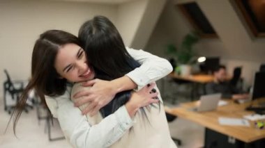 Young female office workers hugging to congratulate a colleague or missing a friend from vacation, slow motion.