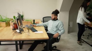 Young businessman working calmly on laptop in office with coworkers around.