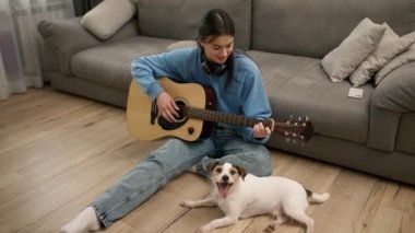 Young girl play the guitar, sitting on the floor with her lovely dog.