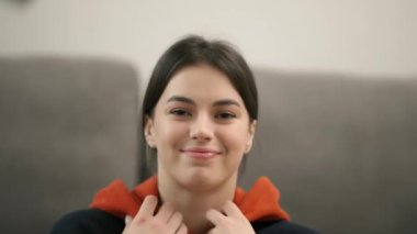 Indoor image of stylish brunette woman dressed in trendy hooded sweatshirt.