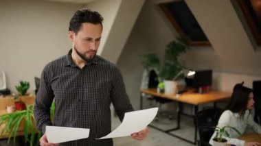 Office worker standing at modern office coworking space holding pile of papers.
