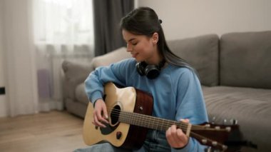 Genç kız gitar çalmayı öğreniyor, yerde kulaklıkla oturuyor..