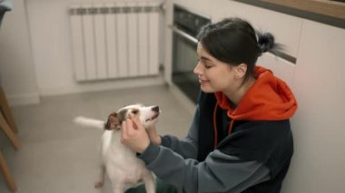 A young girl hugs er small dog in the kitchen, care and love for a pet.