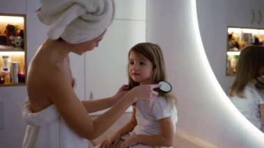 Child and mama brushing hair of young kid in house and getting ready for the day.