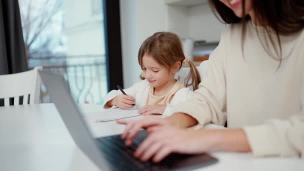 Frau Arbeitet Laptop Während Ihre Tochter Tisch Malt — Stockvideo