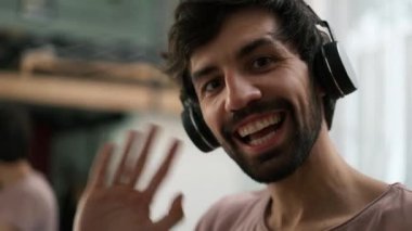 Young man looking at camera in wireless headphones waving to the camera.