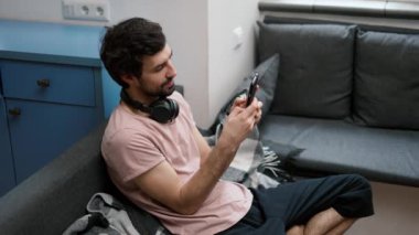 Man on the sofa scrolling on smartphone at home.