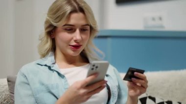 Evde cep telefonu ödemelerini kullanarak kredi kartı tutan mutlu genç bir kadın..