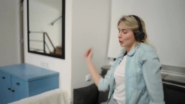 Happy young woman dancing at home having fun listening to music wearing headphones.