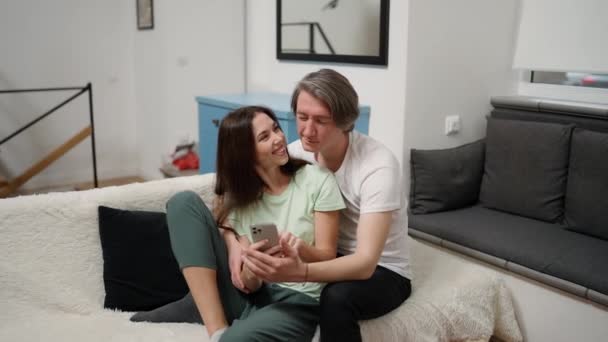 Couple Assis Ensemble Embrassé Sur Lit Utilisant Smartphone Dispositif Défilement — Video