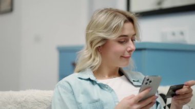 Evde cep telefonu ödemelerini kullanarak elinde siyah kredi kartı tutan mutlu genç bir kadın..