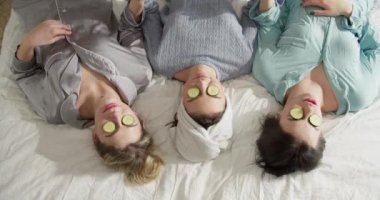 Salatalık maskeli mutlu arkadaşlar kafalarında havlularla yatakta dinleniyorlar..
