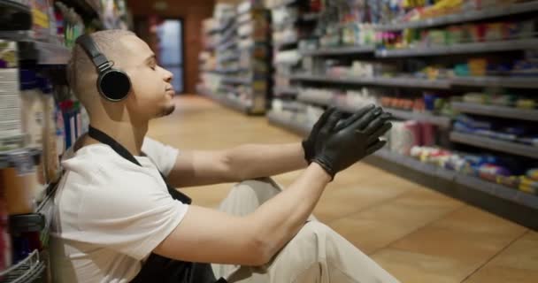 Supermarkt Angestellte Schürze Auf Dem Boden Sitzend Und Musik Hörend — Stockvideo