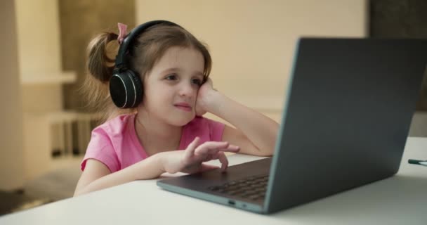 遠くの先生と家からオンラインで勉強ヘッドフォンを身に着けている女の子 — ストック動画