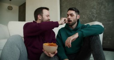 Evde oturup romantik bir konuşma yapan eşcinsel bir çift ortağını cipslerle besler..