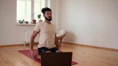 Sakallı sporcu erkek derin derin nefes alıyor, gözleri kapalı oturma odasında egzersiz paspasına oturuyor..