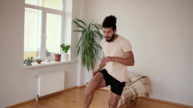 Atletik formda bir adam minimalist iç mekanla evde ileri atlama egzersizleri yapıyor..
