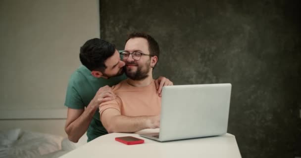 若いです男性抱擁とキスハンサムなボーイフレンド仕事上のラップトップ — ストック動画