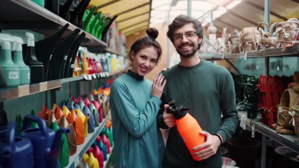 花园商店里拿着橙色喷雾器的一对年轻夫妇的画像 — 图库视频影像