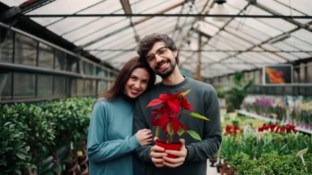 年轻漂亮的一对穿着休闲装的情侣牵着一株植物 看着相机 面带微笑 — 图库视频影像