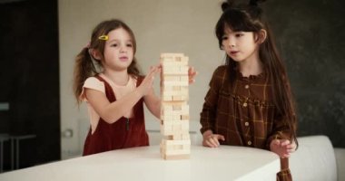İki genç kız arkadaş oyun oynayan çocuklar mutfaktaki masada Jenga oynuyorlar, ağır çekimde..
