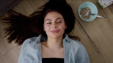 Çekici, uzun saçlı, beyaz tenli, parke üzerinde uzanmış kameraya bakan genç bir kadın..