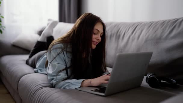 Sorrindo Jovem Mulher Deitada Seu Sofá Digitando Laptop — Vídeo de Stock