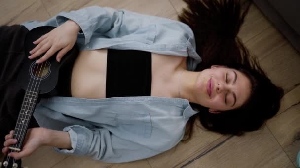 Νεαρή Γυναίκα Παίζει Γιουκαλίλι Στο Σπίτι Ξαπλωμένη Στο Πάτωμα Κοιτάζοντας — Αρχείο Βίντεο