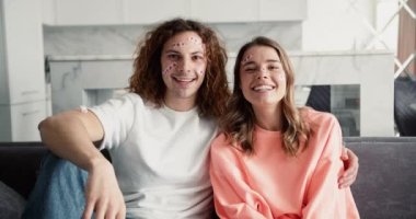 Hoş bir milenyum çifti kanepede oturuyor. Komik, mutlu yüzlü, kalplerinde çıkartmalar olan..